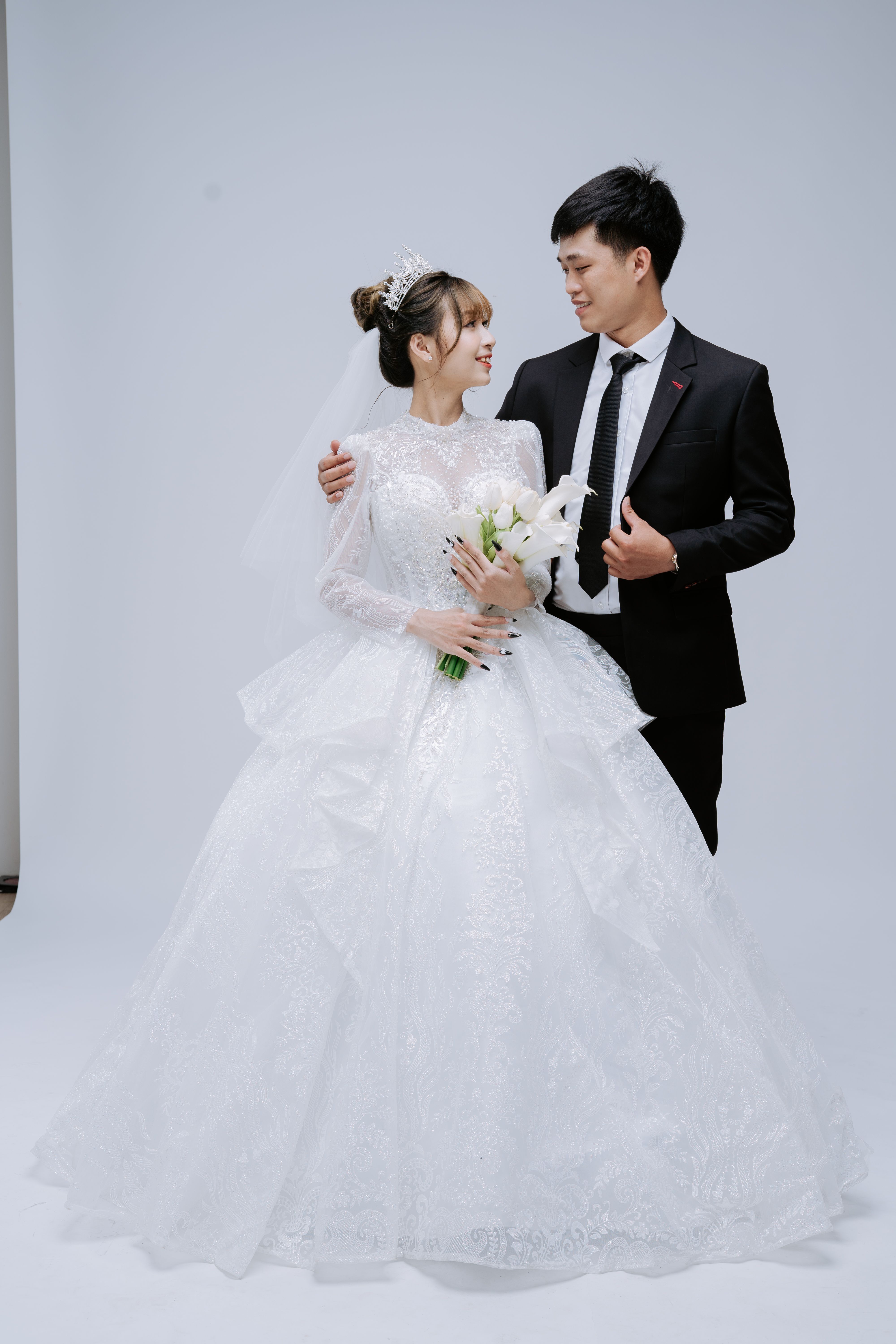 Asian bride and groom in elegant wedding attire posing in a studio setting.