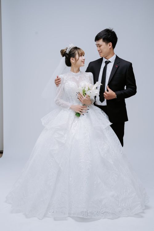 Free Asian bride and groom in elegant wedding attire posing in a studio setting. Stock Photo