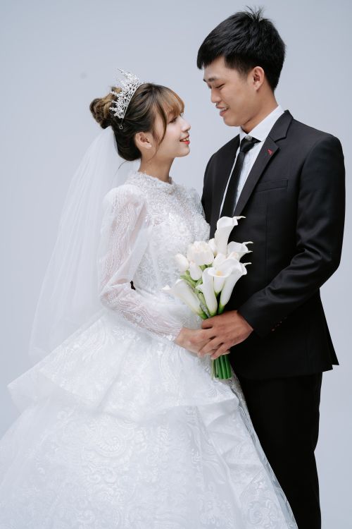 Free Bride and groom in elegant wedding attire smiling at each other in a studio shoot. Stock Photo