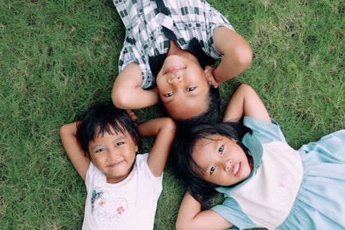 Free Three children lying on grass, enjoying a summer day in Surakarta, Indonesia. Stock Photo