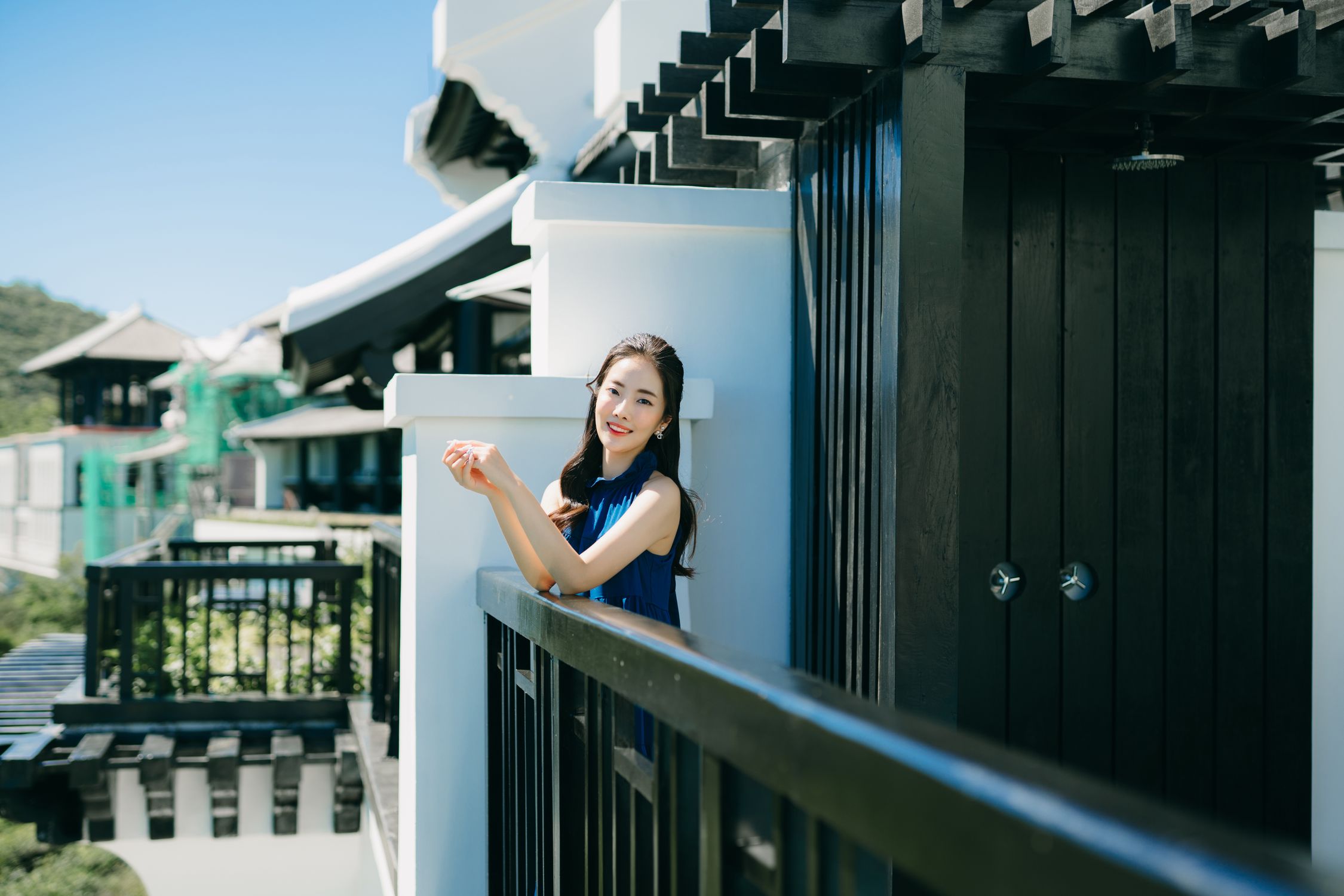 Asian woman with long hair smiling on a modern balcony under clear skies.