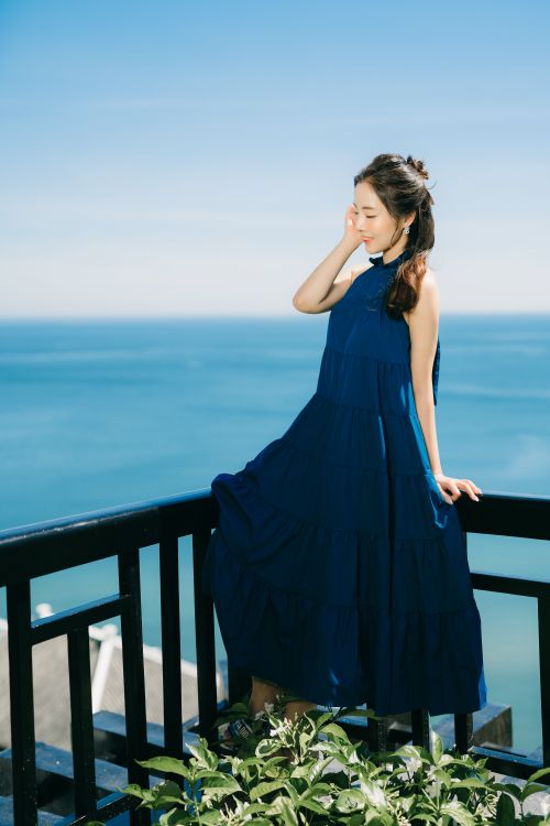 A Woman in a Blue Dress Sitting on a Railing · Free Stock Photo