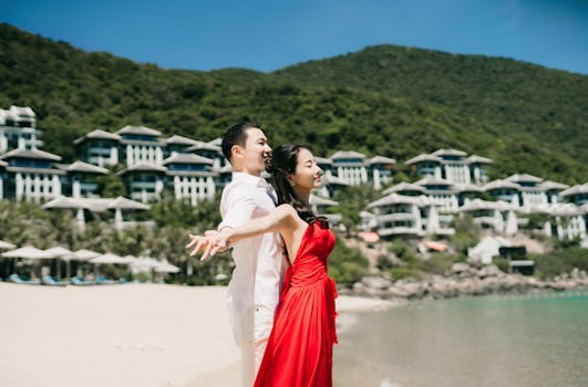 Asian couple in love enjoying a sunny day at the beach with mountains and villas in the background.