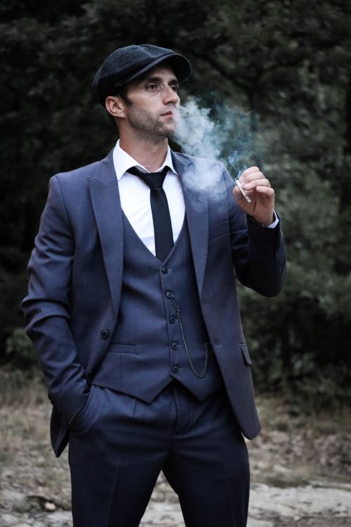 Free Man in a suit with a flat cap smoking outside, conveying a retro style. Stock Photo