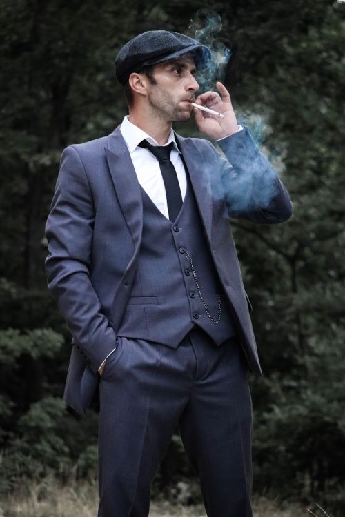 Free Stylish man in a suit and flat cap smoking in a forest setting. Stock Photo