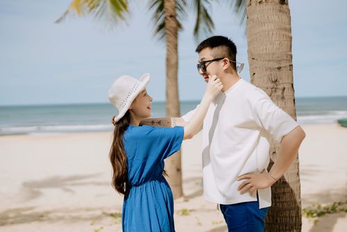 Free An affectionate couple enjoys a playful moment on a sunny beach with palm trees. Stock Photo