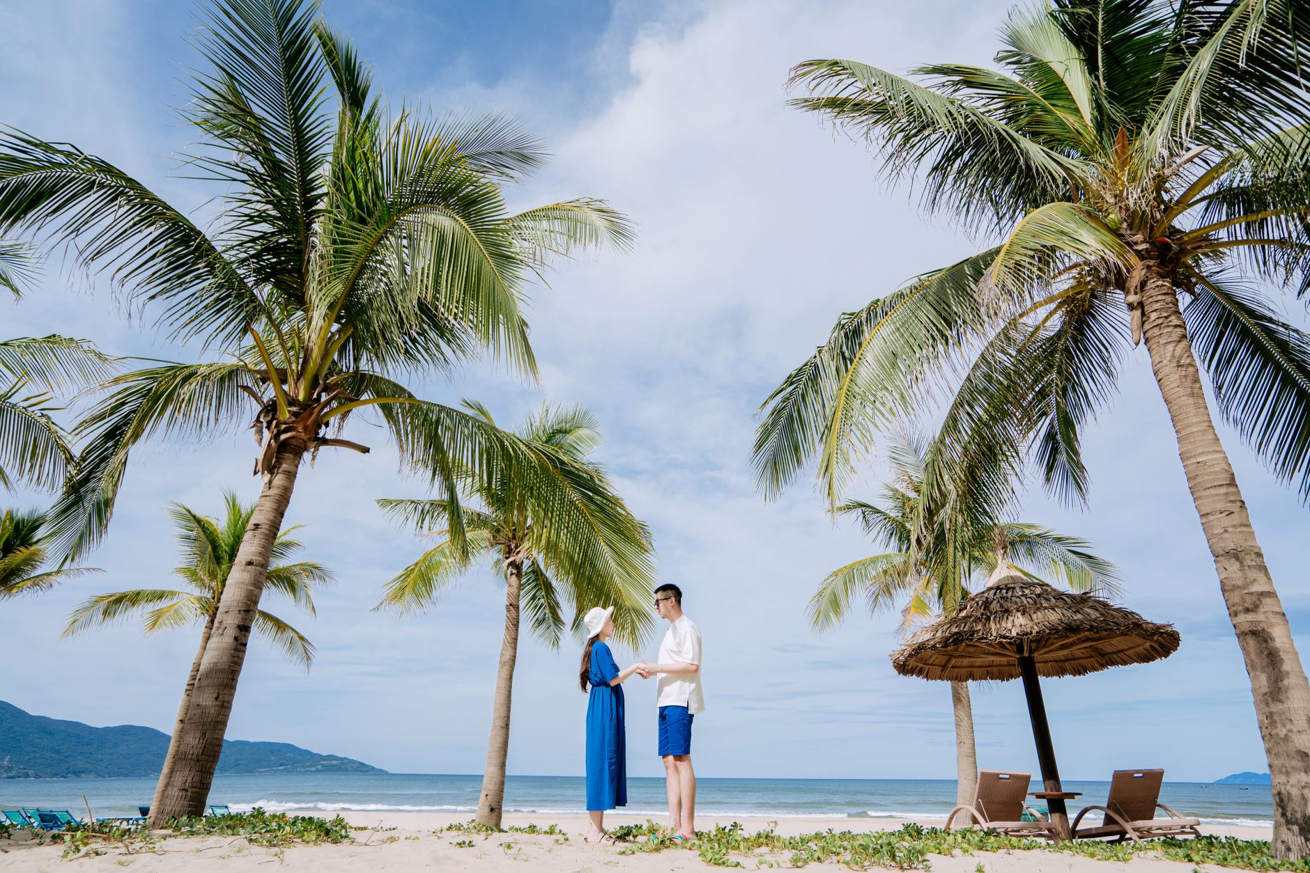 Una pareja se coge de la mano en una playa soleada rodeada de cocoteros, disfrutando de unas vacaciones tropicales.