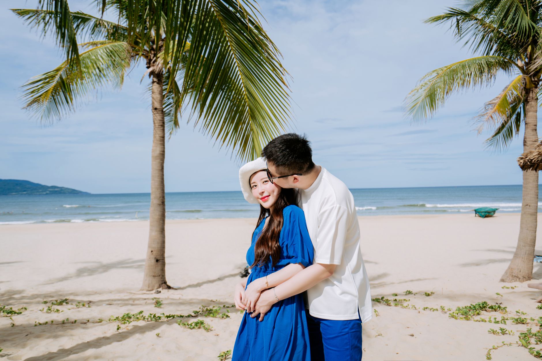 A couple embracing on a sunny beach with palm trees, exuding love and serenity.