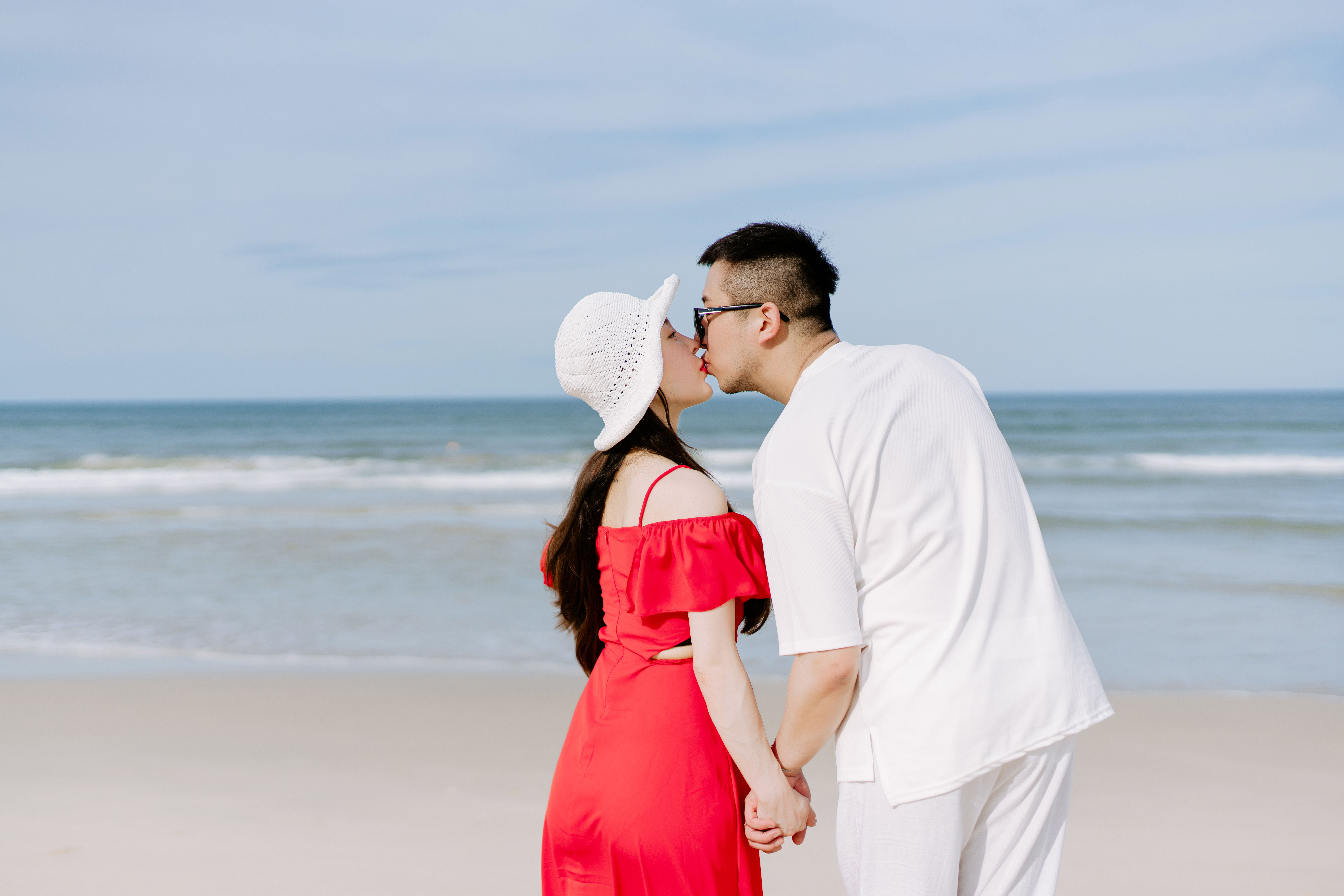 A couple shares a romantic kiss on a sunny beach, symbolizing love and connection.