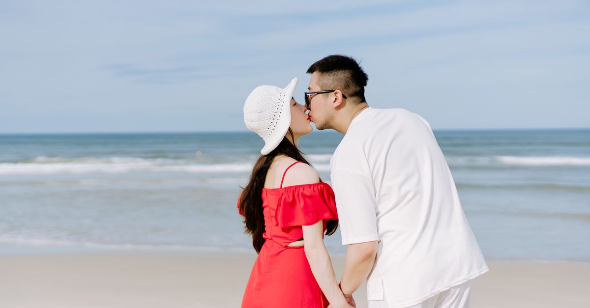 A couple shares a romantic kiss on a sunny beach, symbolizing love and connection.