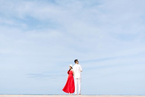 Free A couple in red and white outfits walking on a sandy beach under a clear blue sky. Stock Photo