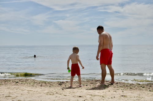 Free Man in Red Shorts Standing Beside Boy in Red Shorts on Beach Stock Photo