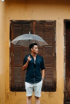 Casual man standing with an umbrella by rustic shutters on a summer day.