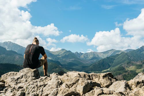 Free Man Sitting on Rocks Within Mountain Range Stock Photo