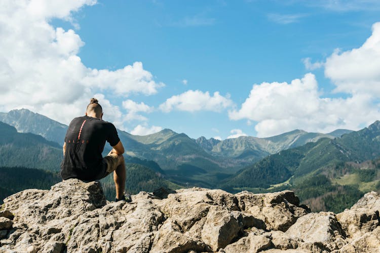 Man Sitting On Rocks Within Mountain Range