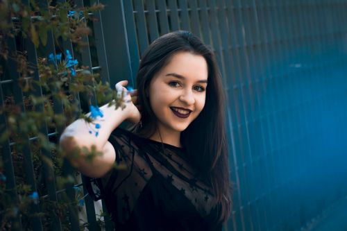 Free A cheerful young woman poses near a blue fence, showcasing vibrant style. Stock Photo
