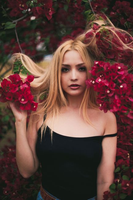 Portrait of a blonde woman amidst vivid red flowers, capturing natural beauty and elegance.