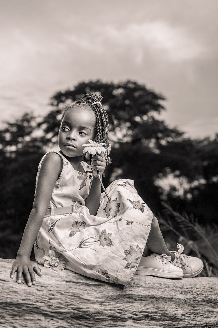 A Girl Holding Flower While Sitting On Tree Log