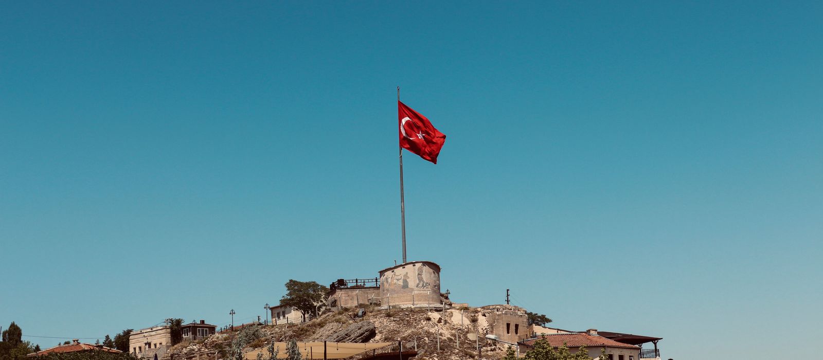 The Turkish flag waves proudly atop a hill in Avanos, Nevşehir against a bright blue sky.