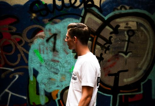 Side profile of a young man in a white t-shirt walking past a colorful graffiti wall.