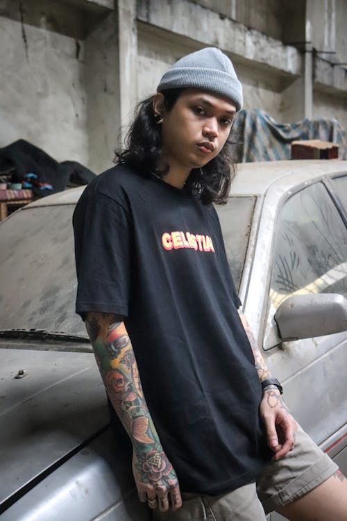 Young Man with a Tattoo on his Arm Leaning against a Car 