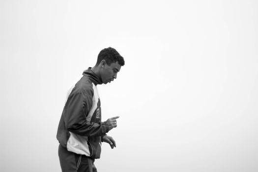 Black and white profile portrait of a man in a tracksuit captured outdoors.