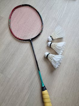Badminton racket with three shuttlecocks on a wooden floor, perfect for sport and recreation concepts.
