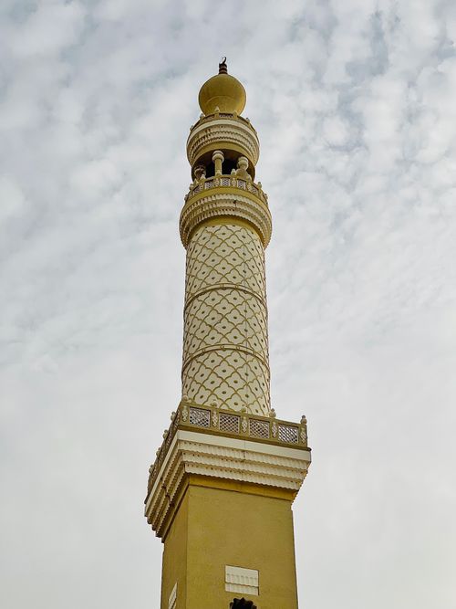 Free A beautifully ornate golden minaret of an Islamic mosque set against a cloudy sky. Stock Photo