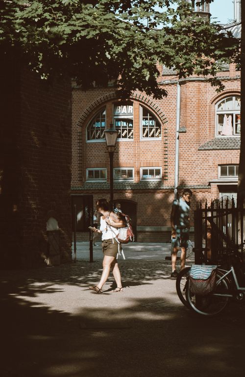 Free A summer street scene with people walking by brick buildings and bicycles, in warm sunlight. Stock Photo