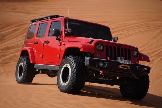 A vibrant red Jeep Wrangler navigating rugged desert dunes, perfect for adventure enthusiasts.