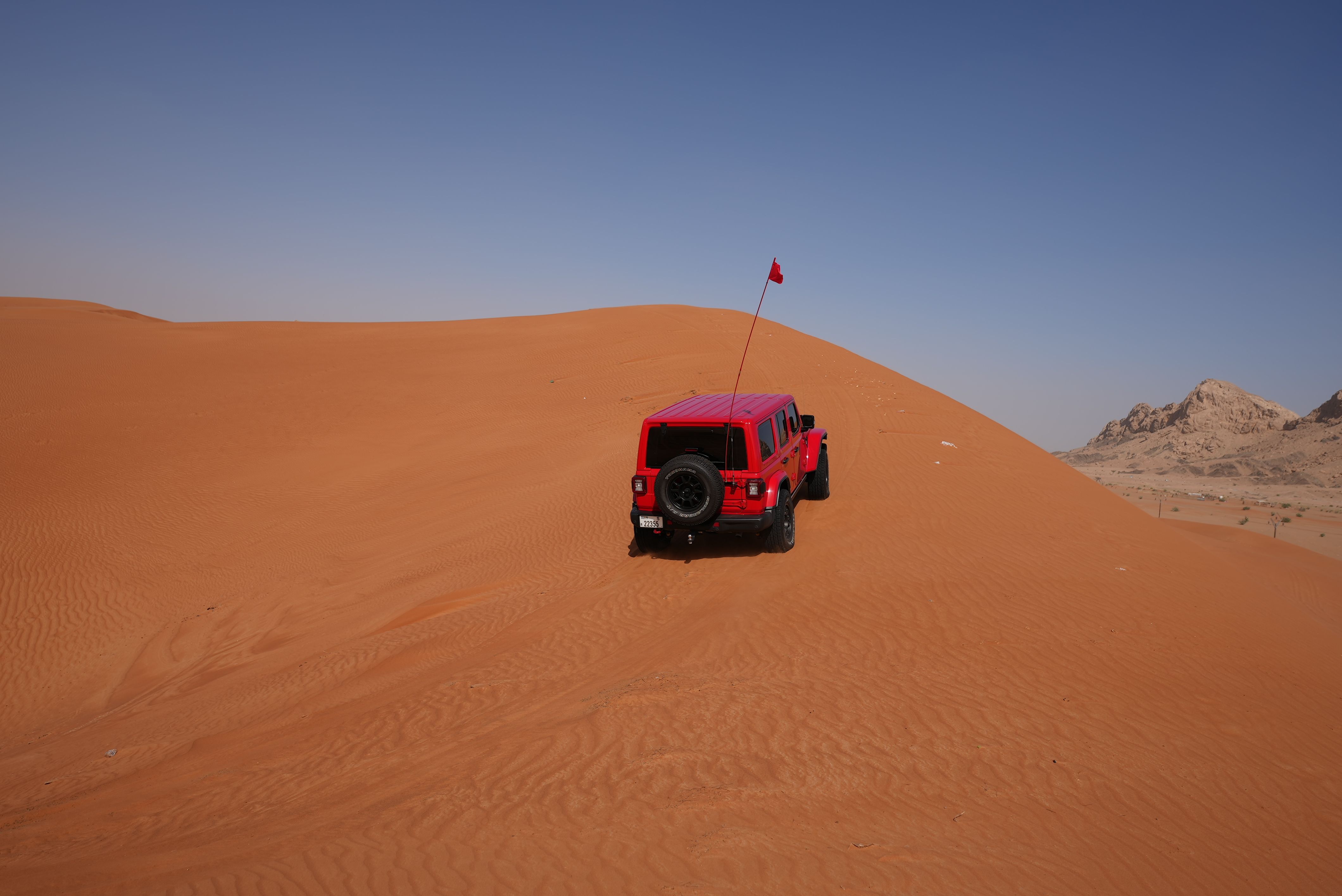 Red SUV driving over desert dunes under a clear blue sky, capturing adventure and travel.