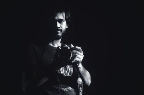 Free Black and white portrait of a bearded man holding a camera with dramatic lighting. Stock Photo