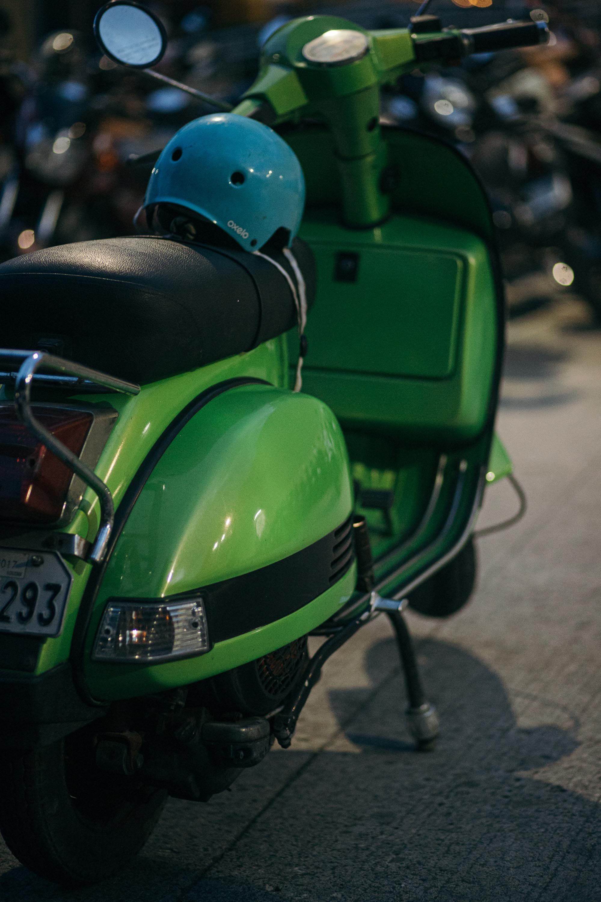 Green scooter parked on pavement with blue helmet under streetlights at night.