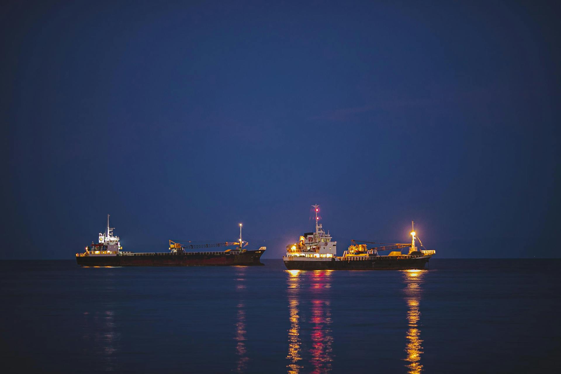 Illuminated cargo ships reflecting on the calm sea at sunset, capturing maritime industry serenity.