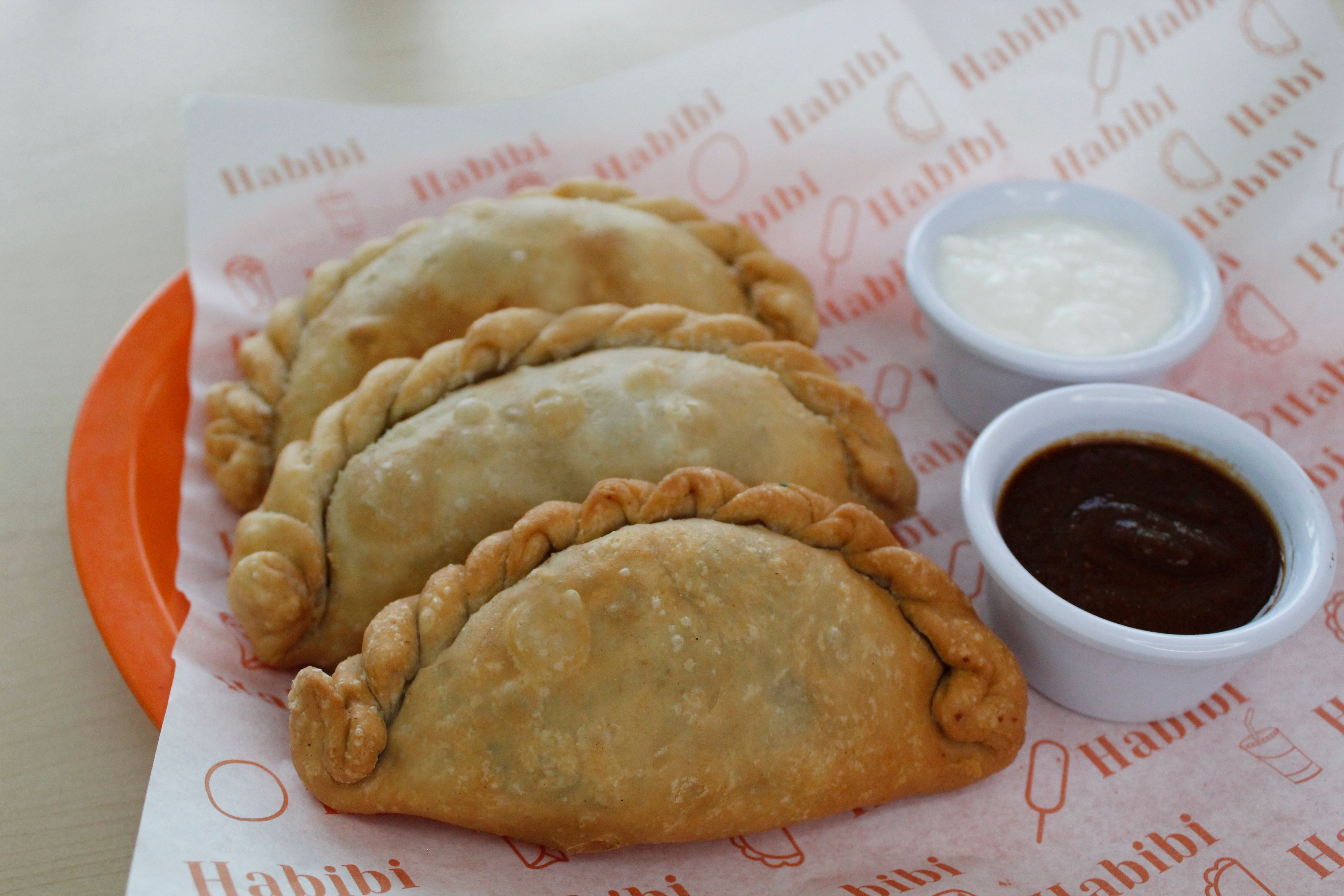 Freshly baked empanadas served with flavorful white and brown dips on a vibrant plate.