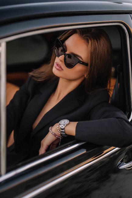 Elegant woman wearing sunglasses, seated in a luxury car, exuding style and sophistication.