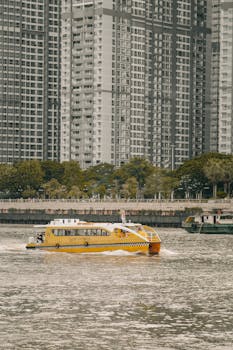 Yellow water taxi on a river with skyscrapers in Ho Chi Minh City.