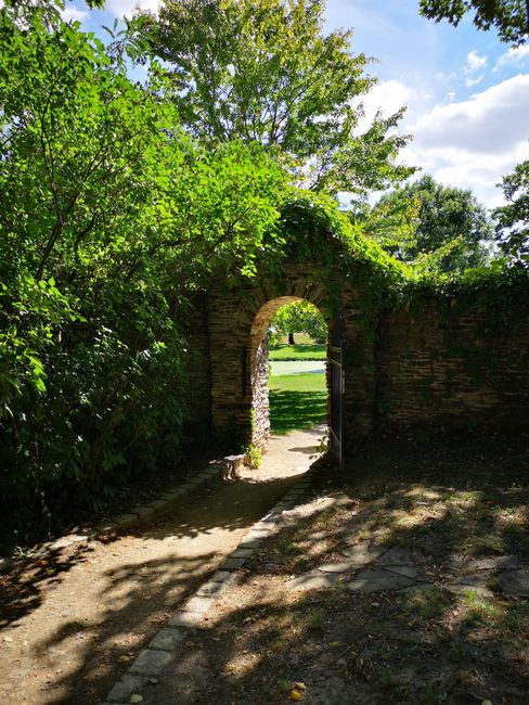 A charming stone gate surrounded by lush greenery under a clear blue sky in a garden.