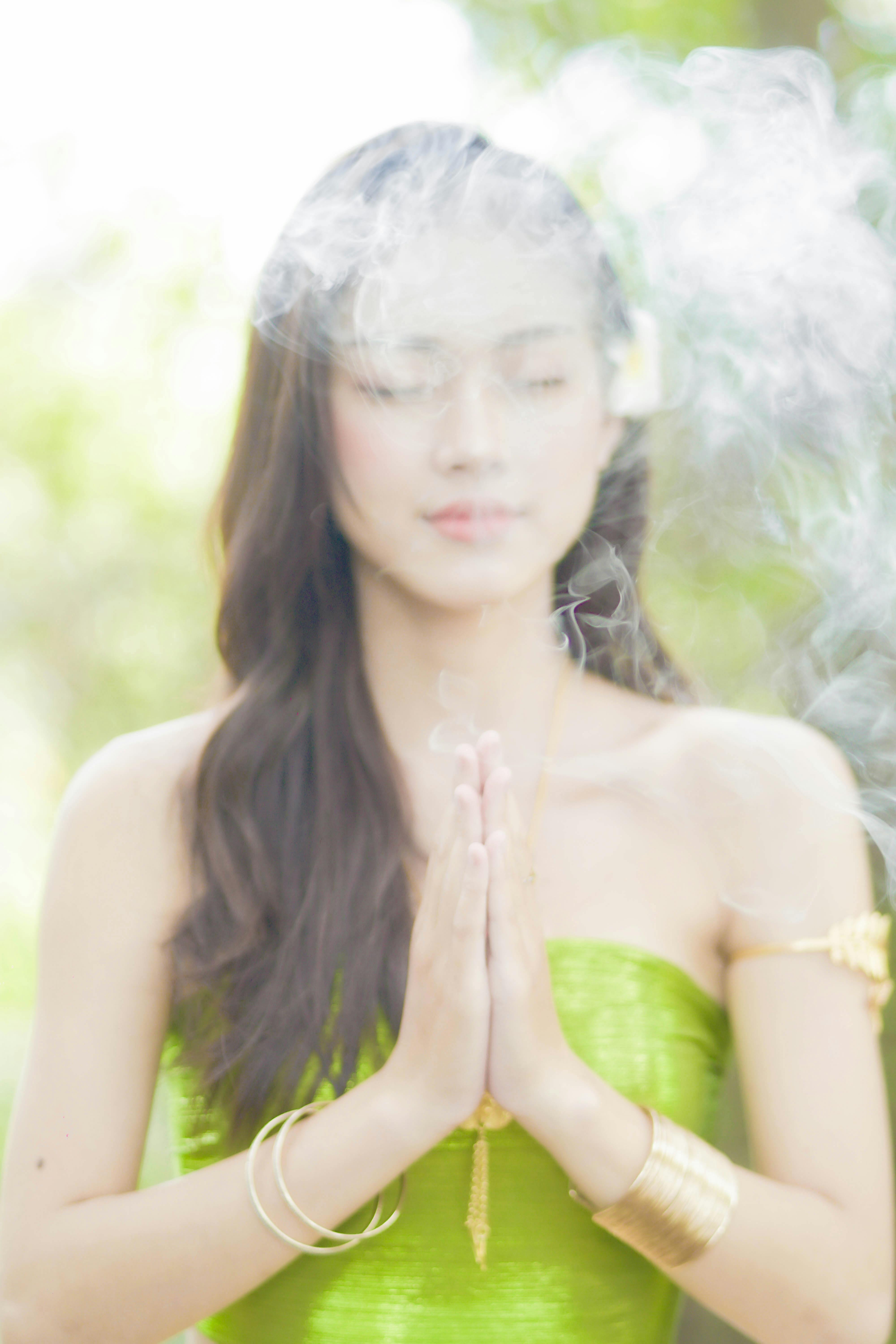 Serene woman meditating with hands together, eyes closed, surrounded by smoke outdoors.