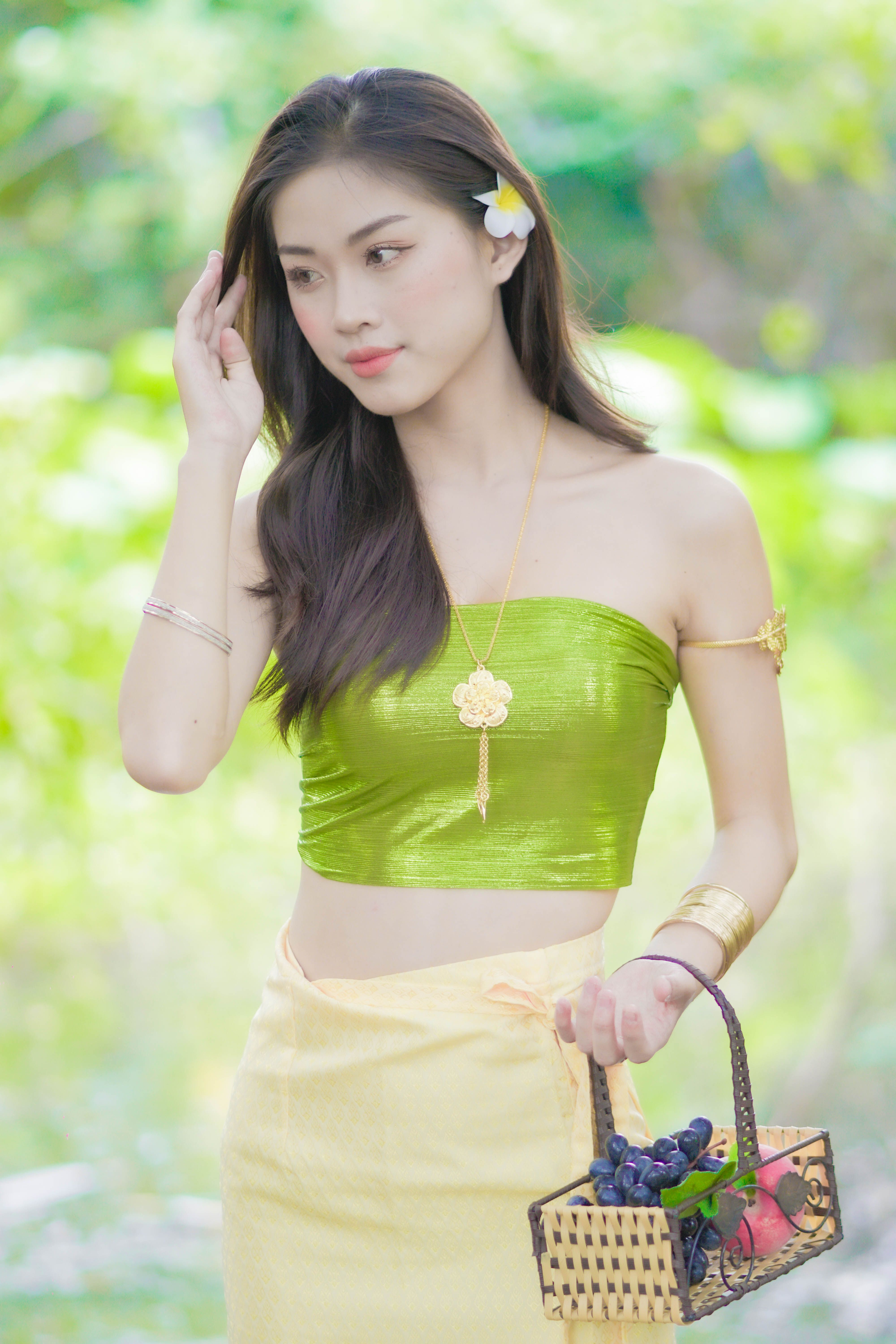 Asian woman in vibrant green attire holding a basket of fruits outdoors.