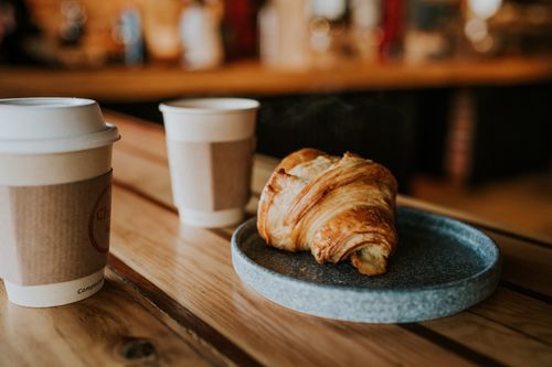 Free Cozy café setting with paper cup coffee and fresh croissant on a wooden table. Stock Photo