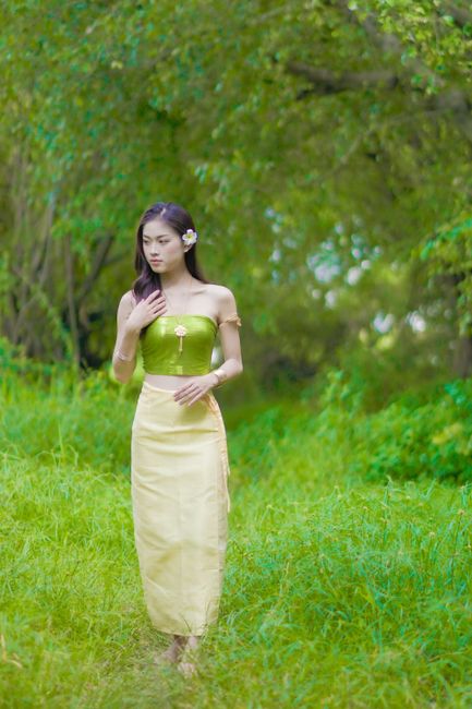 A woman in vibrant traditional attire strolls through a verdant forest path surrounded by lush greenery.