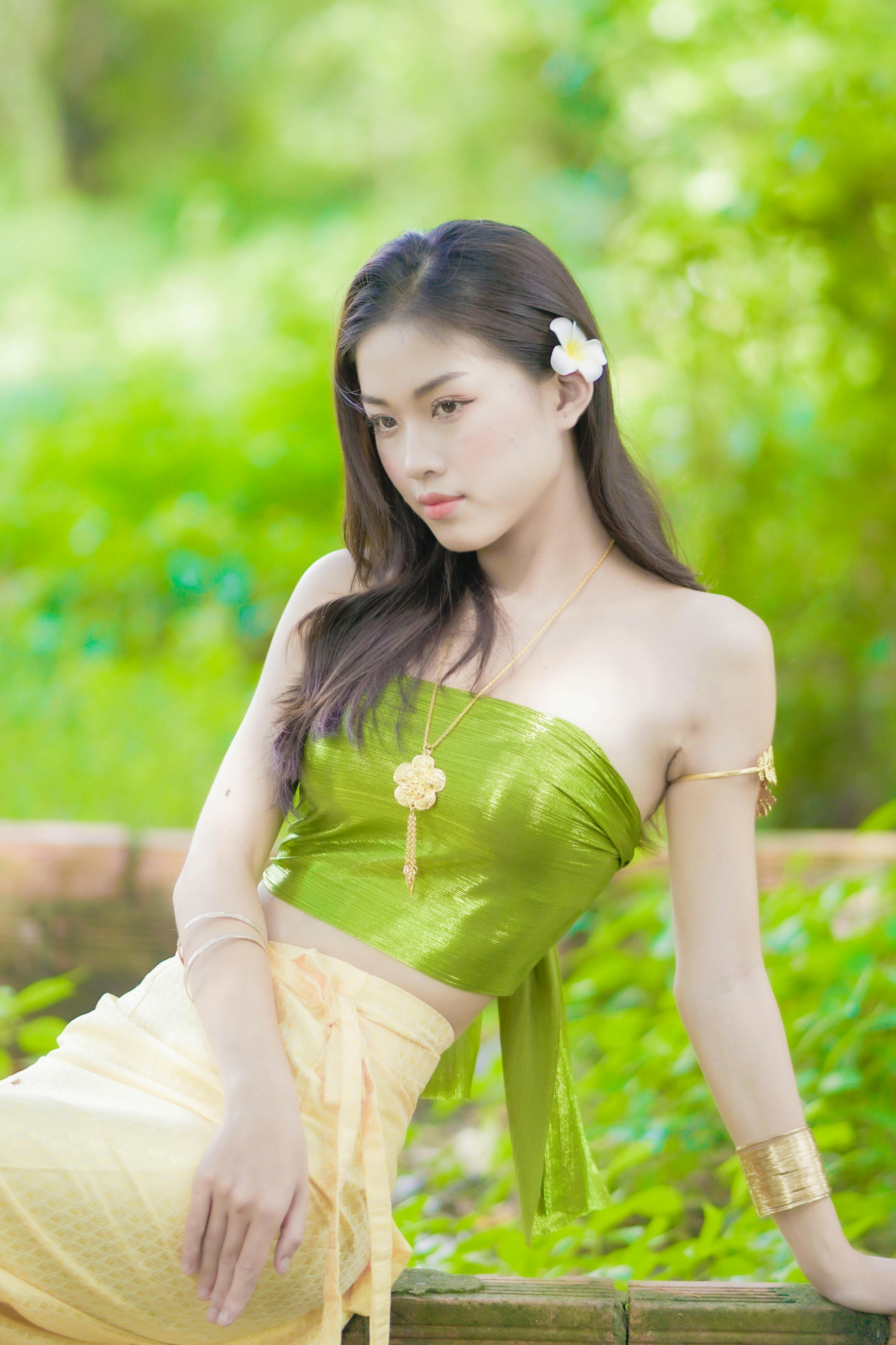 A graceful Asian woman in a green tube top poses beautifully outdoors in a fashion photoshoot.