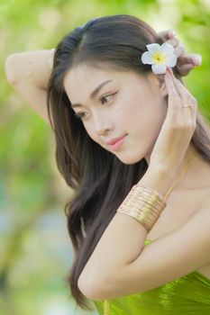 Close-up of a woman fixing her hair with a white flower in a natural outdoor setting.