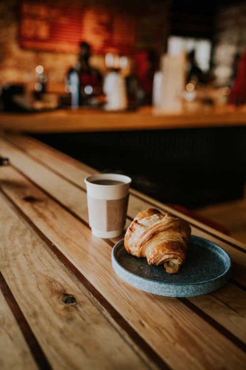Free Cup of coffee and croissant on a wooden table in a cozy café setting. Warm ambiance. Stock Photo