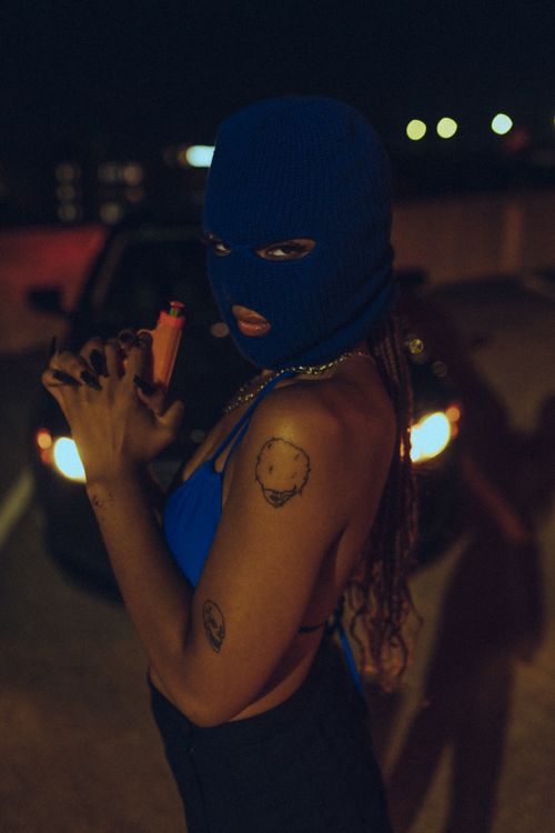 Free A woman wearing a balaclava poses with a toy gun on a city street at night. Stock Photo