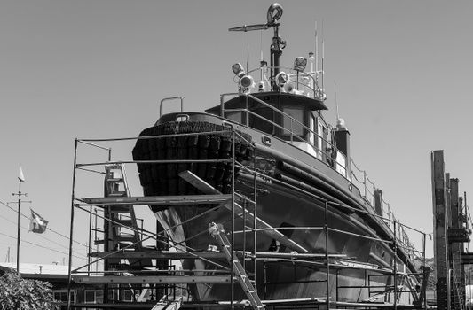 Photo by David McElwee Monochrome image of ship undergoing repairs in a shipyard, showcasing industrial scaffolding.