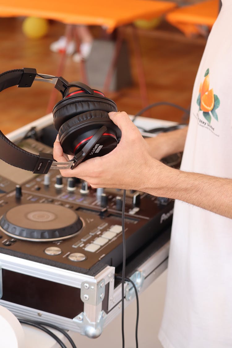 Person Holding A Black Headphone Beside A Dj Mixer