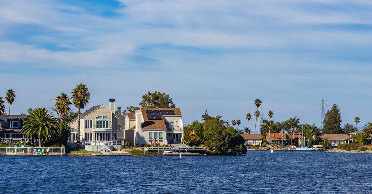 Charming waterfront homes with palm trees and solar panels reflecting in blue water.