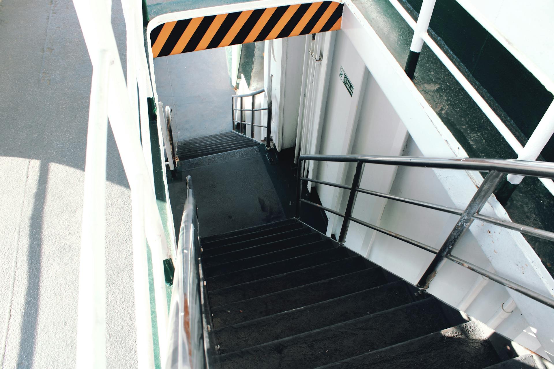 Steep metal stairway on a ship's deck with a caution barrier and white walls.